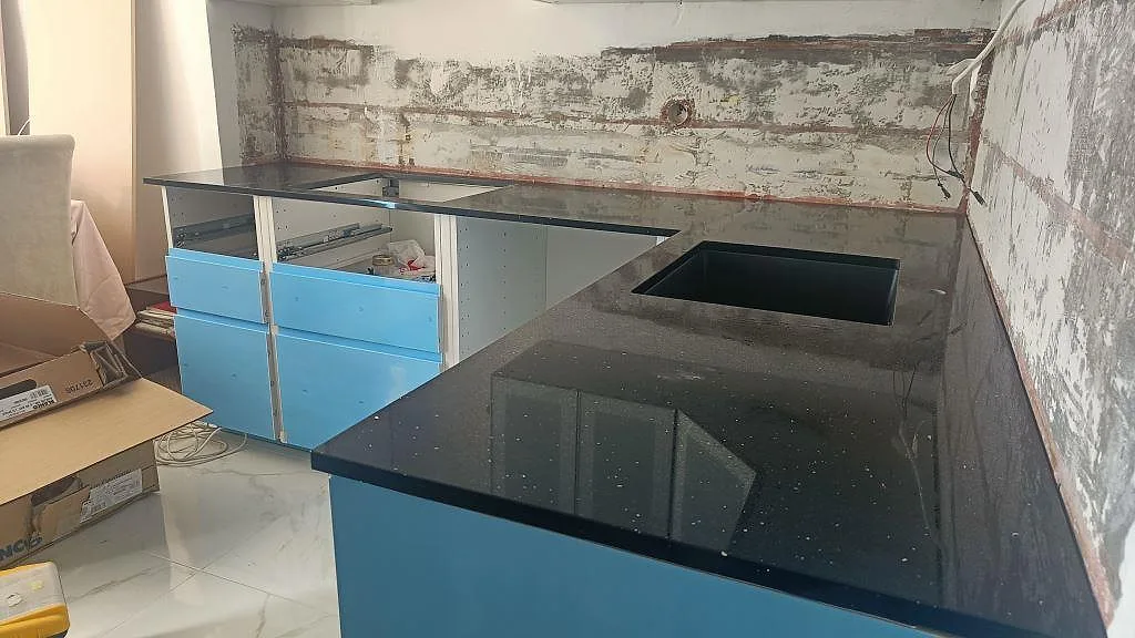 Köksbänkskiva i svart Technistone Starlight Black kvartskomposit, polerad med fint silverglitter, L-formad bänk med tomt hällurtag i ett kök under montering i Malmö.
