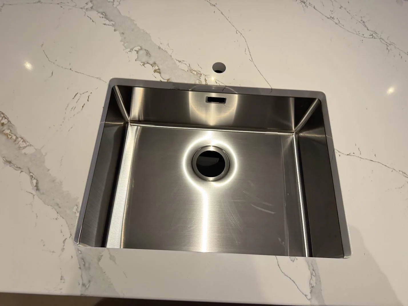 Närbild på en underlimmad diskho i rostfritt stål monterad i en köksbänkskiva av Technistone Volegno med grå ådring i Skovlunde.