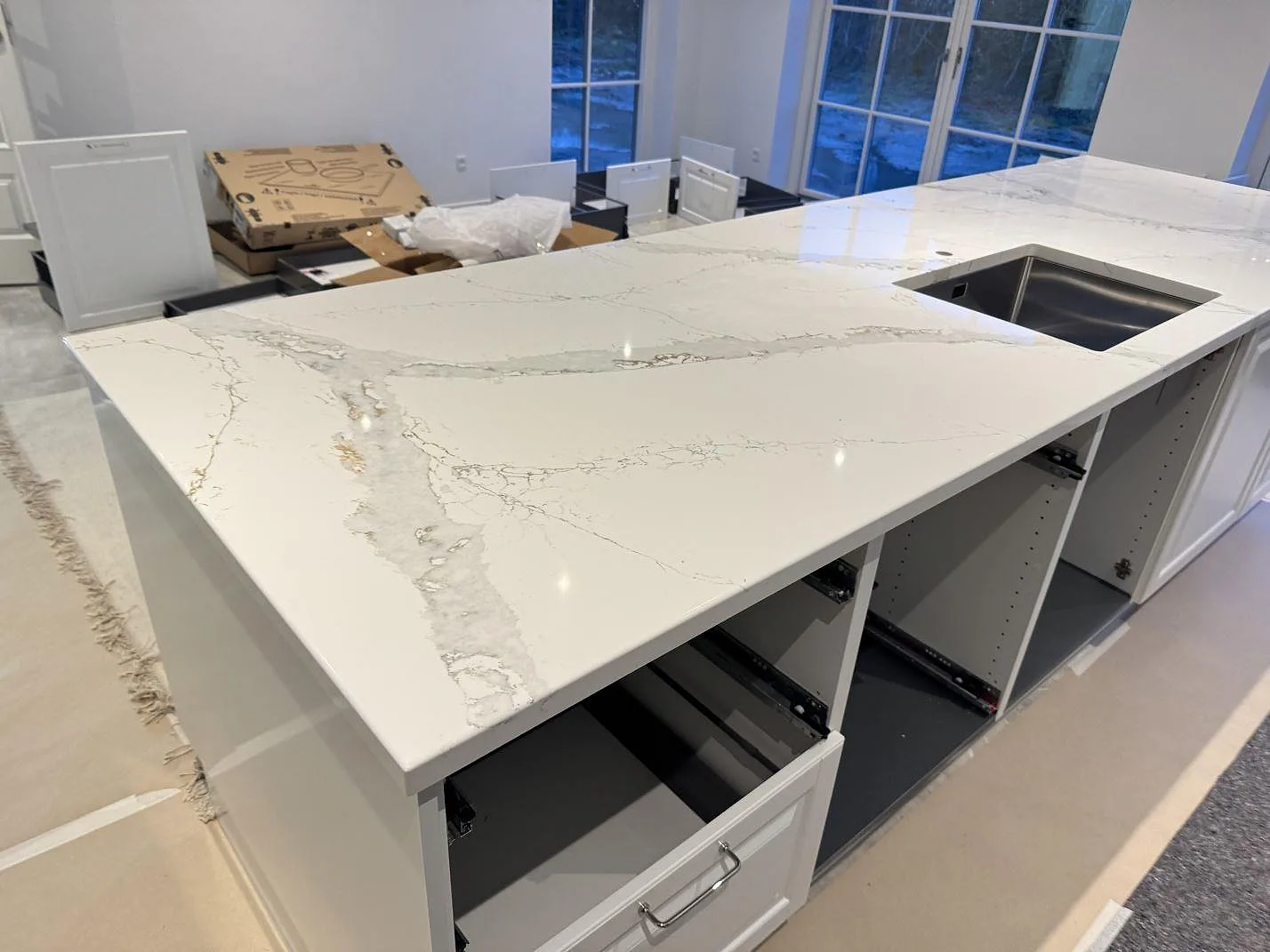Lång köksö i Technistone Volegno med polerad yta och underlimmad rostfri diskho, fotograferad mot fönstren innan köket var helt inrett i Skovlunde.