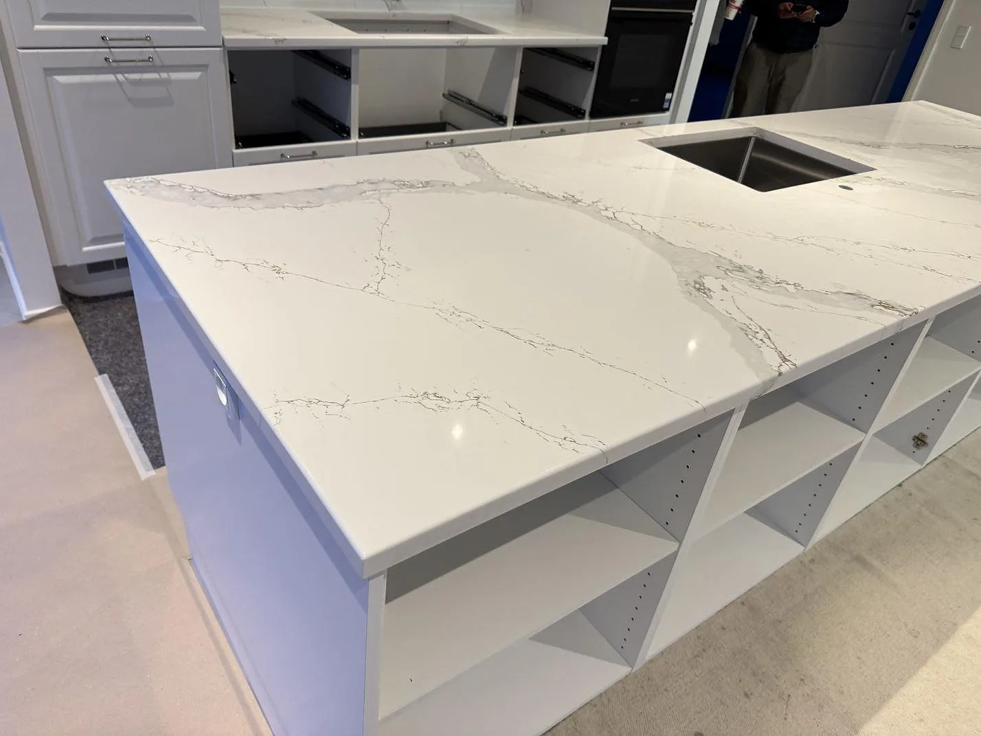 Köksö i polerad Technistone Volegno med underlimmad rostfri diskho och bänkrad i bakgrunden, i ett kök under montering i Skovlunde.