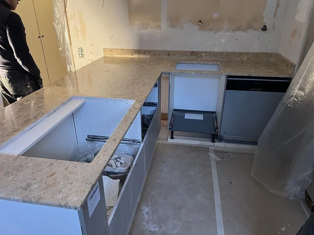 Närbild av matt Terrazzo Breccia Oniciata på köksö med hoöppning, hällplats och uppvikt stänkkant under montering i Stockholm.