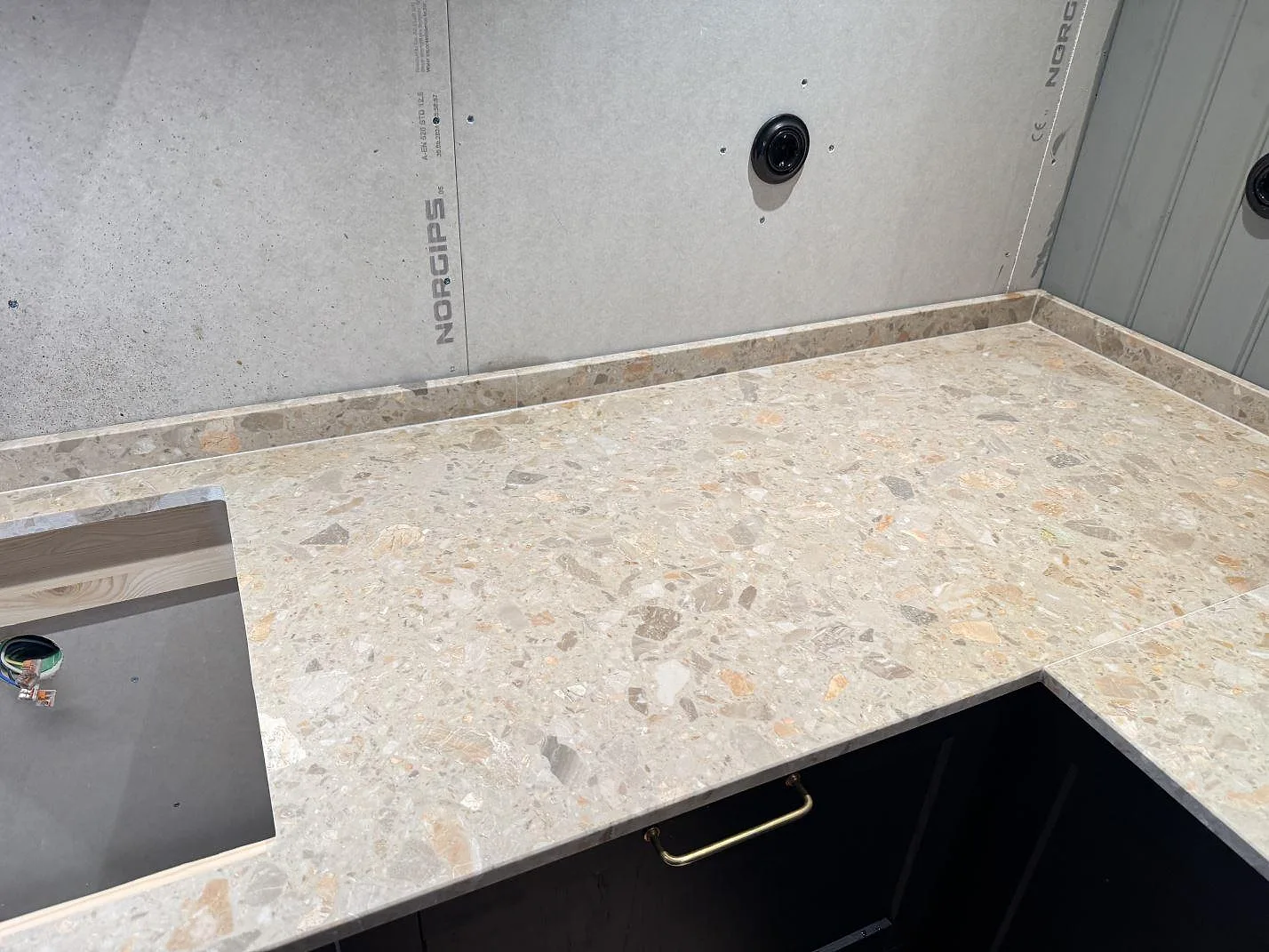 L-formad köksbänkskiva i Terrazzo Breccia Oniciata, matt, med låg stänkkant och utskärning för häll i Tomelilla.