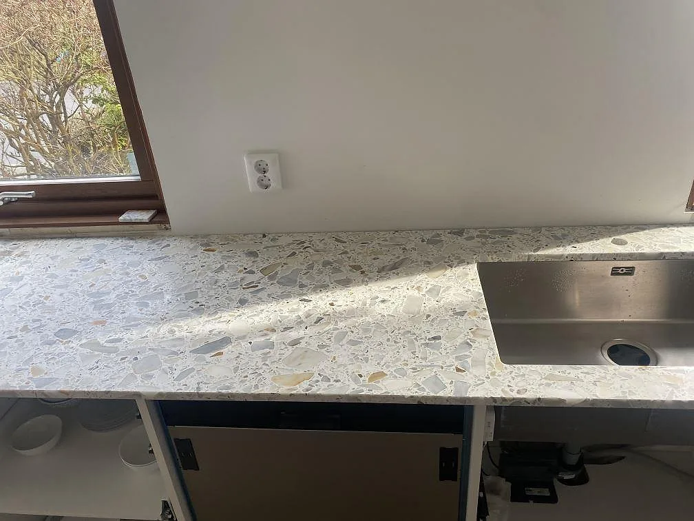 Köksbänkskiva i vit Terrazzo Calacatta med krossad marmor, matt yta, och underlimmad rostfri diskho i ett kök i Bjärred.