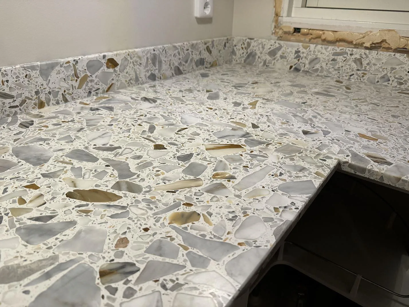 Detaljbild av matt Terrazzo Calacatta i hörn med uppvikt stänkkant och vit köksvägg i Förslöv.