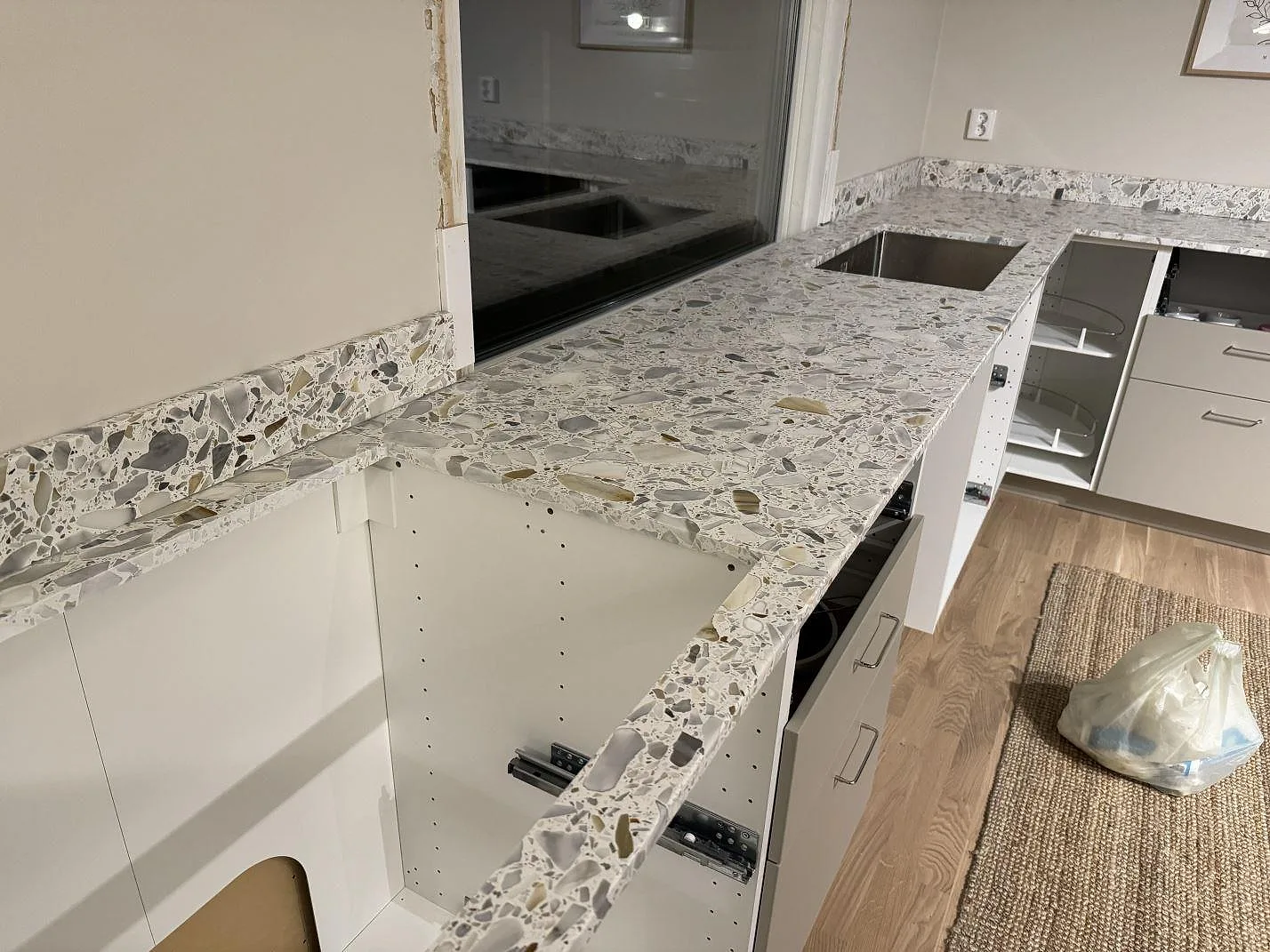 Köksbänkskiva i matt Terrazzo Calacatta med uppvikt stänkkant och diskbänksdel i ett kök i Förslöv.