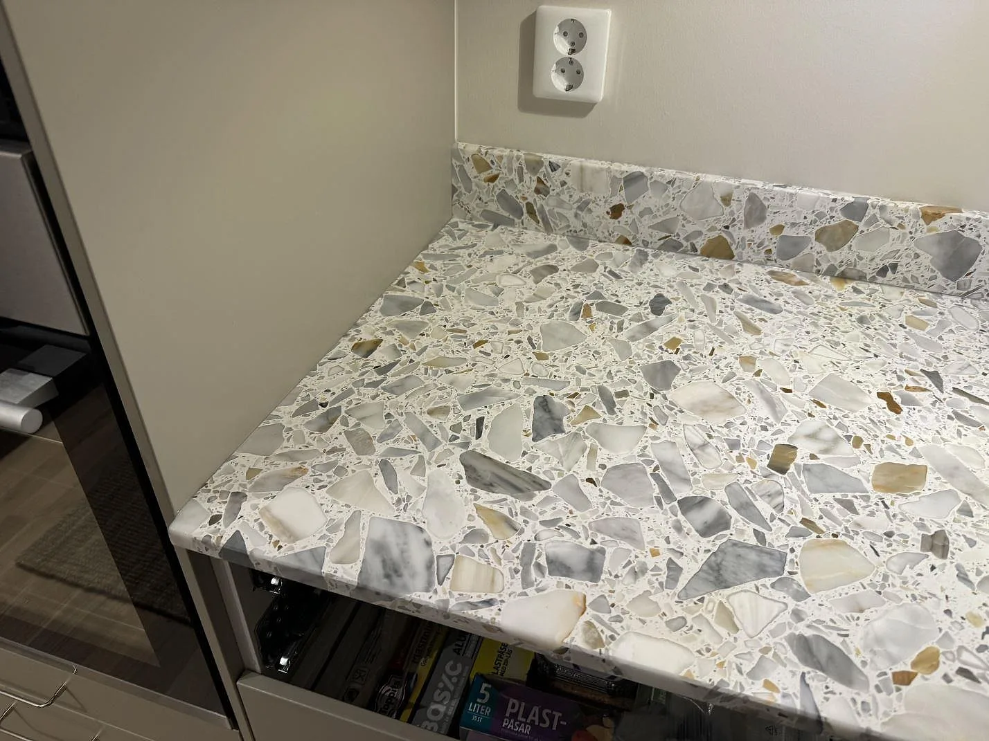 Köksbänkskiva i matt Terrazzo Calacatta med uppvikt stänkkant och vita köksstommar i Förslöv.