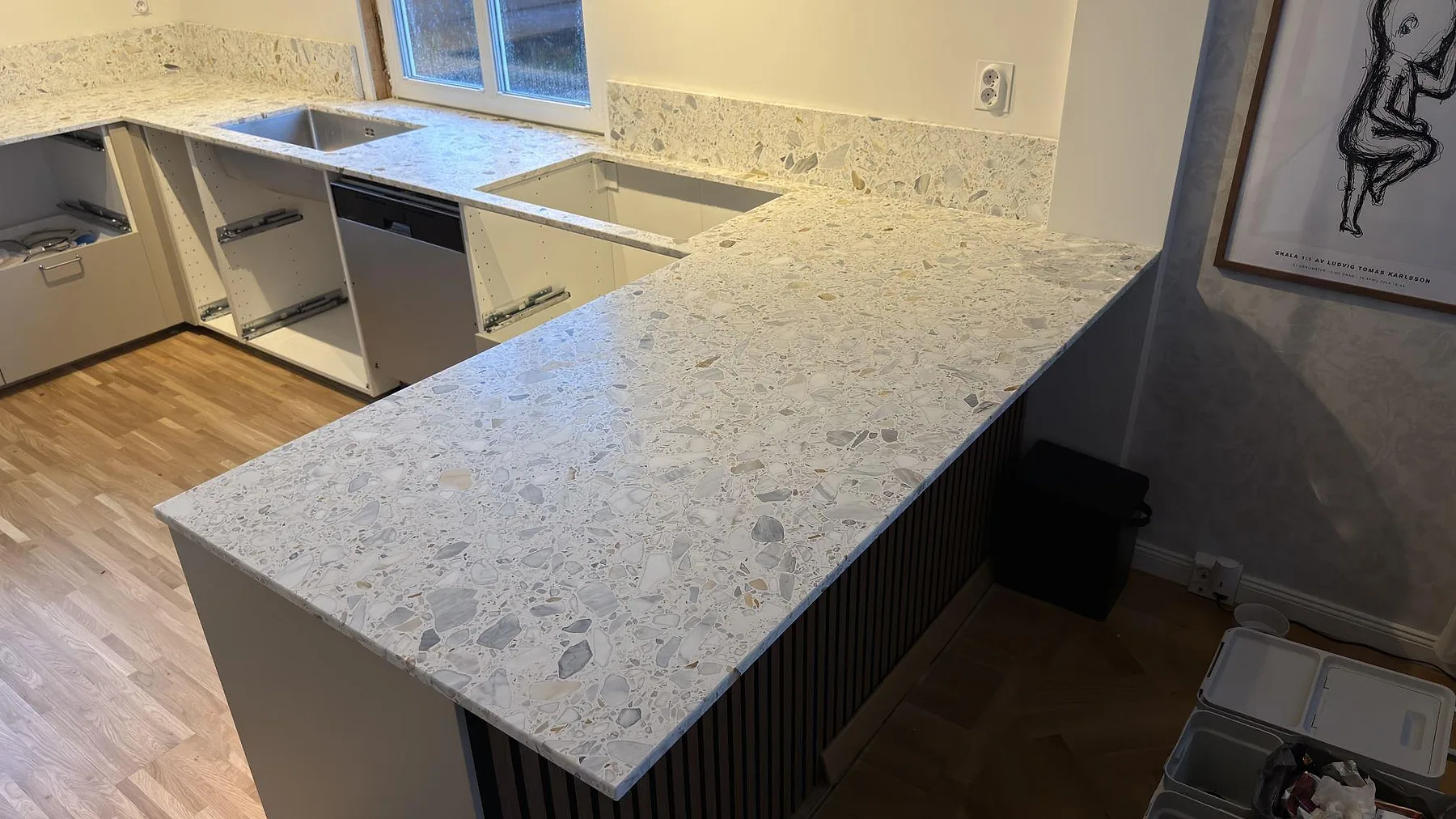 Närbild på den matta Terrazzo Calacatta-bänkskivan på köksöns halvö, med grov grå och cremefärgad terrazzoflis, i ett kök i Karlskoga.