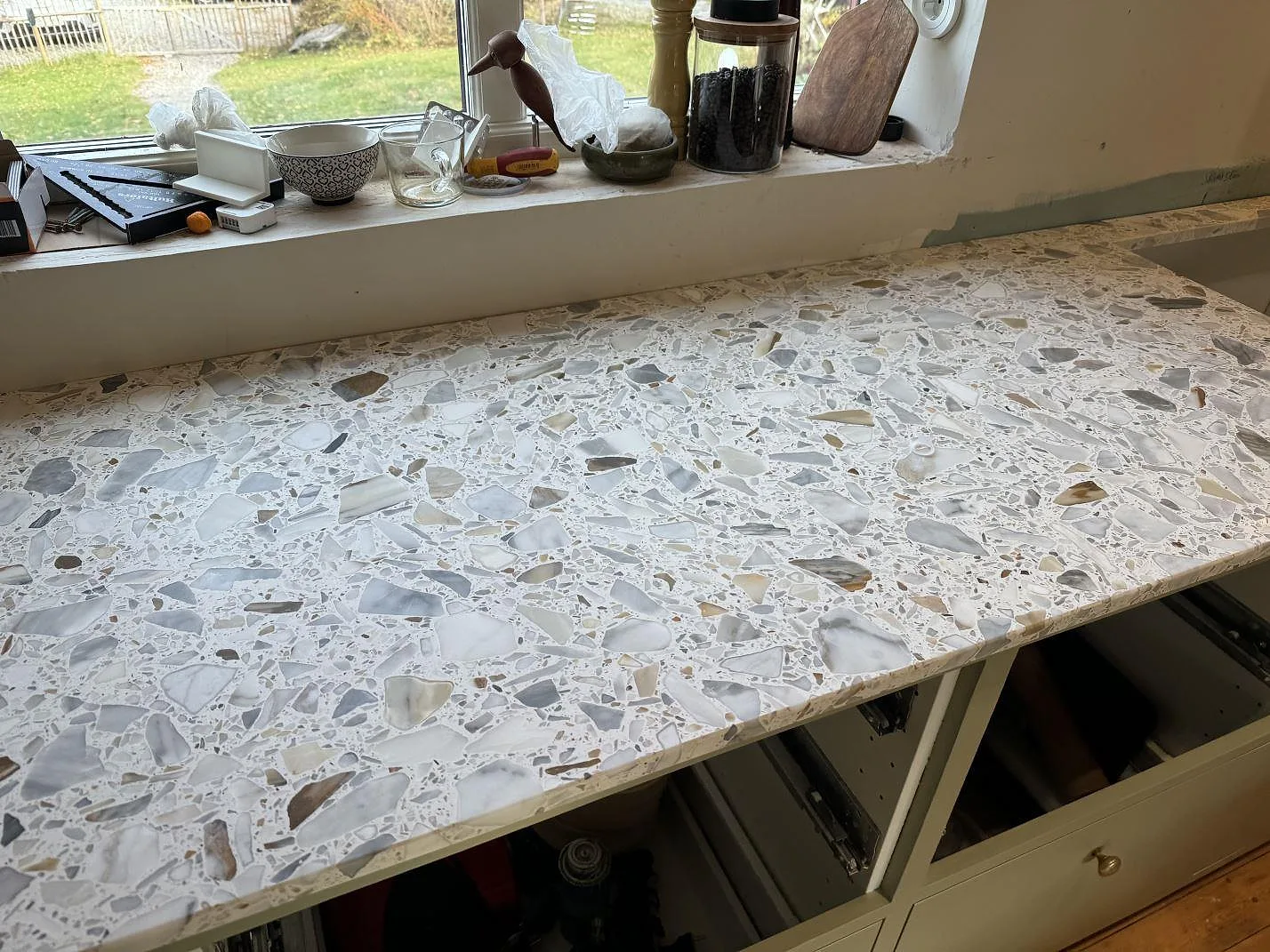 Ytbild av matt Terrazzo Calacatta som köksbänkskiva under fönster, med grå och beige stenflis i Kode.