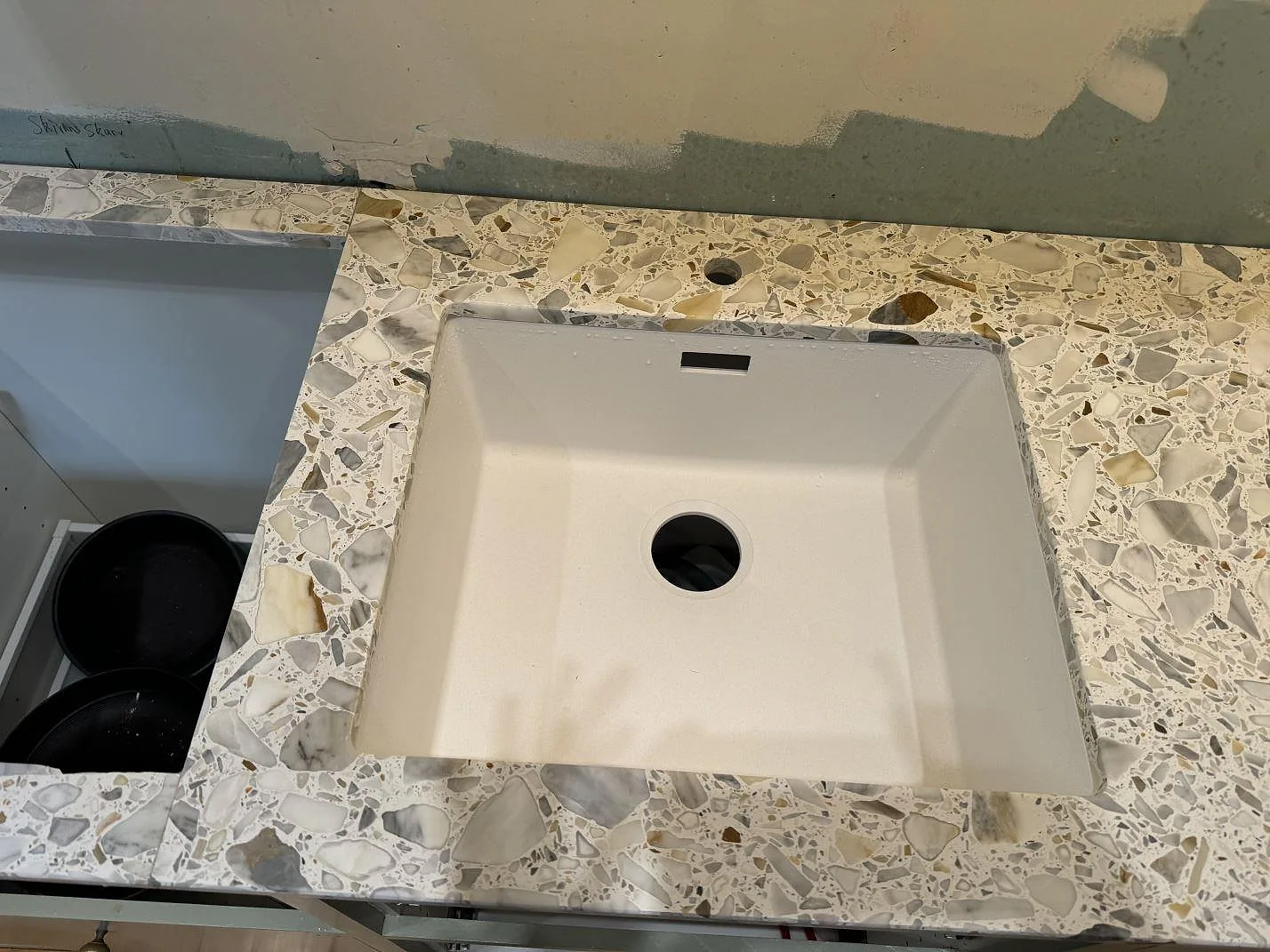 Köksbänkskiva i matt Terrazzo Calacatta med vit diskho och synligt blandarhål under montering i Kode.