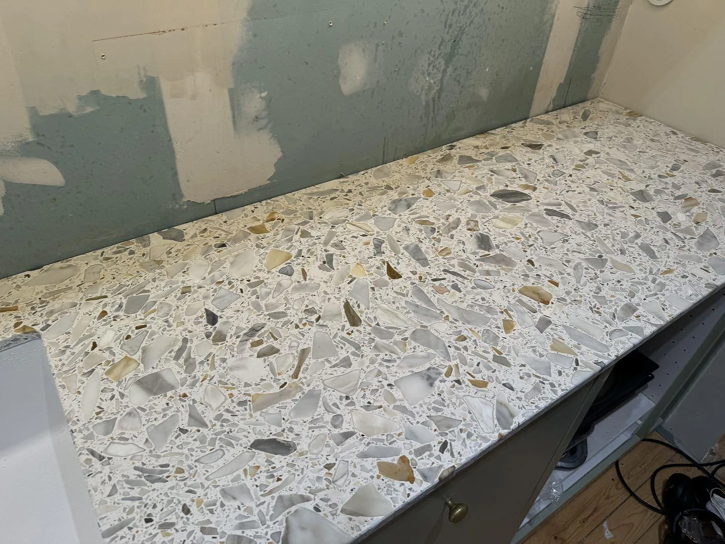 Rak del av köksbänkskivan i matt Terrazzo Calacatta mot oavslutad vägg under montering i Kode.