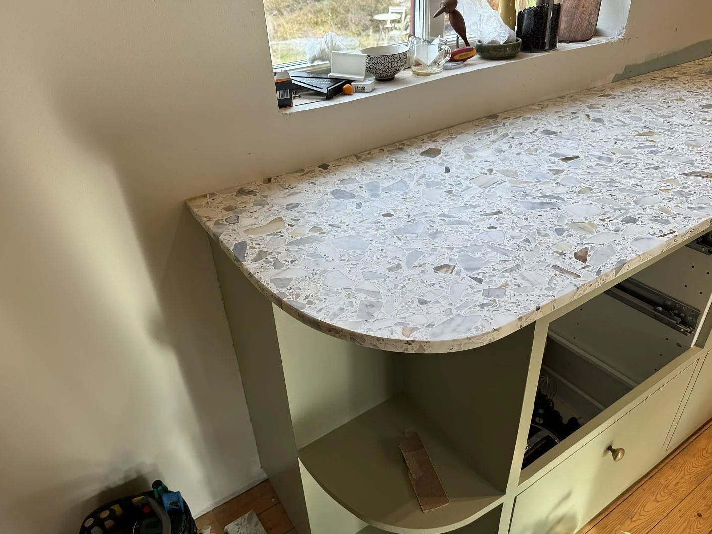 Närbild av rundad köksbänkskiva i matt Terrazzo Calacatta med ljus terrazzo och öppna köksstommar i Kode.