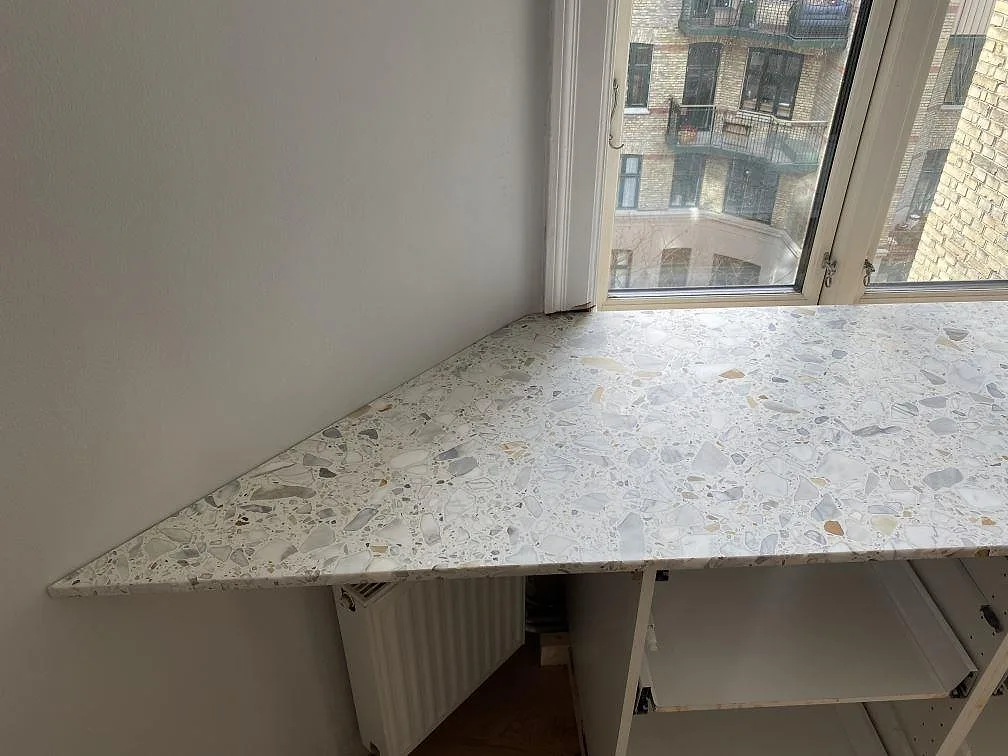 Vänster del av köksbänkskivan i matt Terrazzo Calacatta med synliga terrazzo-fragment vid fönster i København Ø.