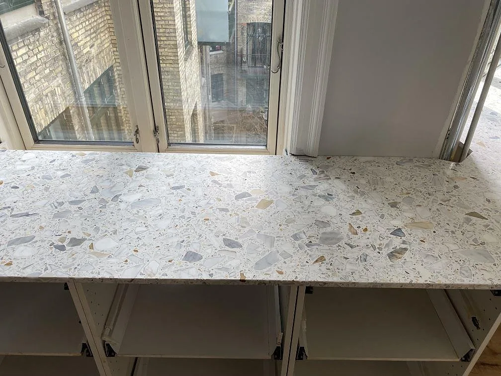 Detalj av den matta Terrazzo Calacatta bänkskivan med ljusa stenfragment framför fönster i København Ø.