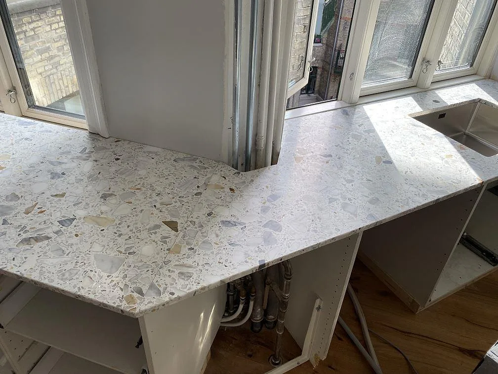 Matt köksbänkskiva i Terrazzo Calacatta med hörnpassning och diskdel framför fönster i København Ø.