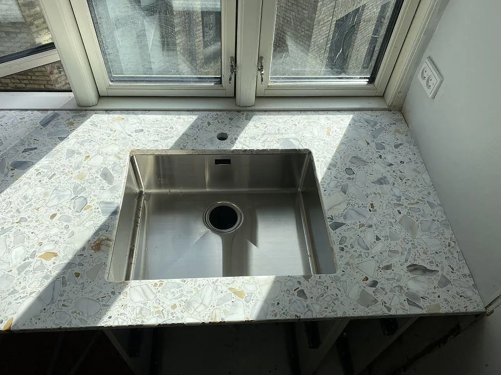 Närbild på Terrazzo Calacatta, matt, runt diskhon och det runda hålet vid fönster i ett kök i København Ø.