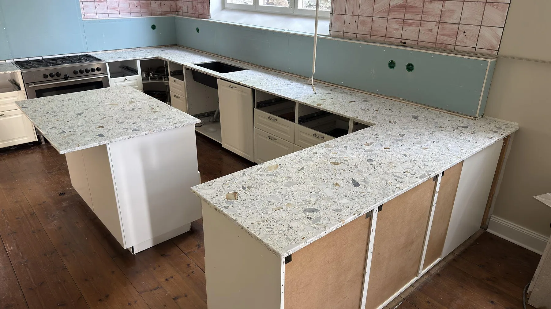 Terrazzo Calacatta bänkskiva som löper längs väggarna i ett U-format kök i Stockholm, fotograferat under montering.
