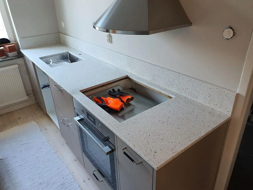Köksbänkskiva i ljus Terrazzo Carrara, matt, med underlimmad diskho, hällurtag och stänkskydd i ett kök i Hägersten.