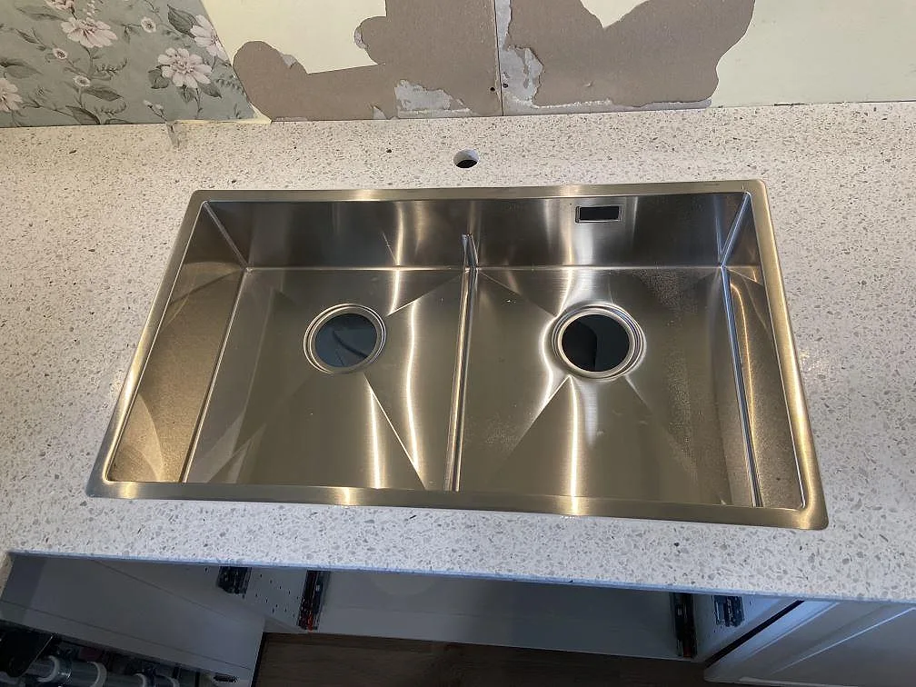 Köksbänkskiva i ljus Terrazzo Carrara, matt, med underlimmad rostfri dubbelho sedd uppifrån i ett kök i Ramdala.