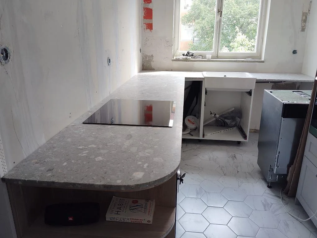 Köksbänkskiva i matt Terrazzo Fior Di Pesco, 20 mm, med rundad halvö, häll och vit lantlig diskho i ett kök i Hägersten.