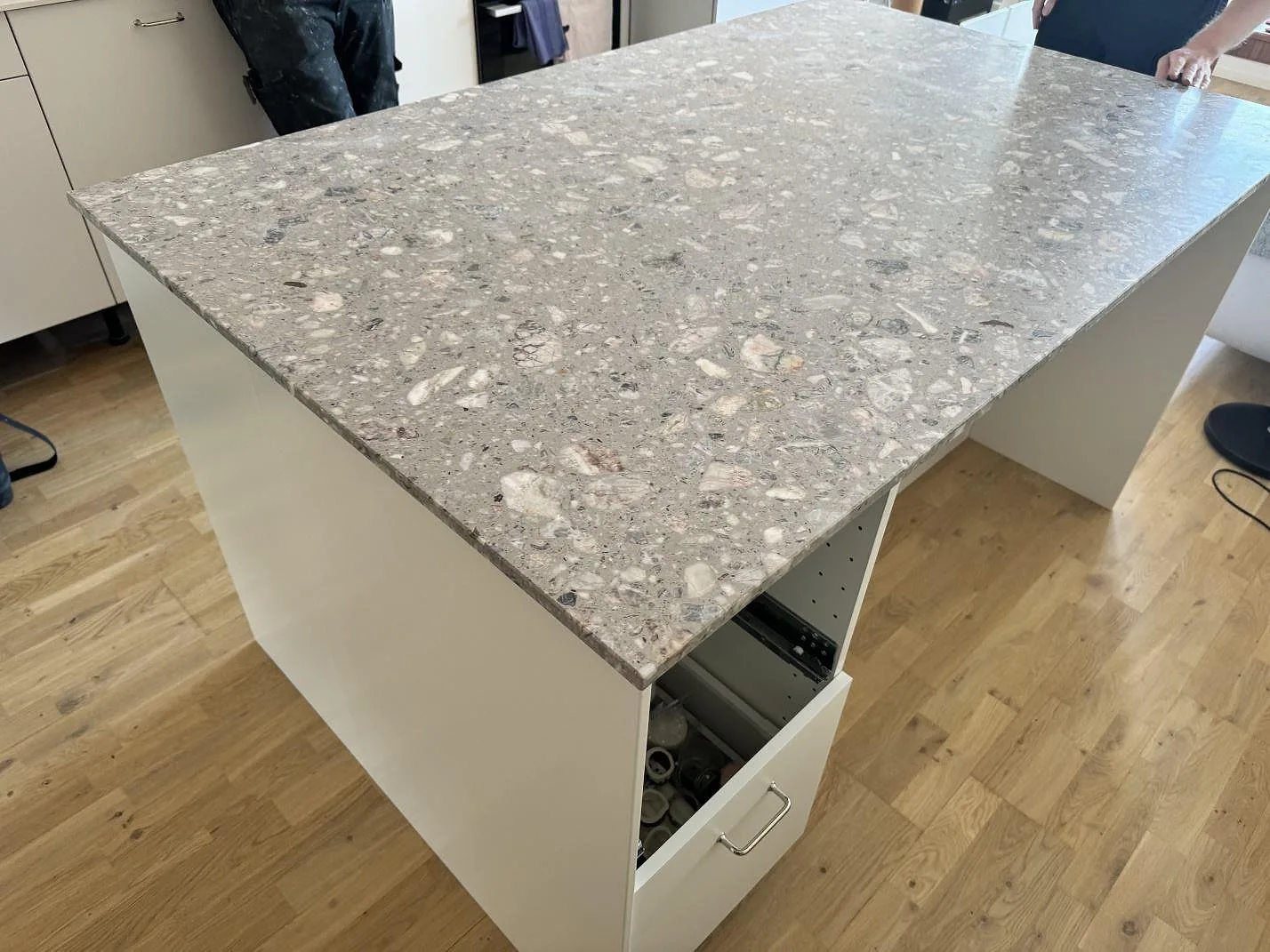 Närbild av den matta terrazzoskivan Terrazzo Fior Di Pesco på en vit köksö i Malmö, med öppen låda under montering.