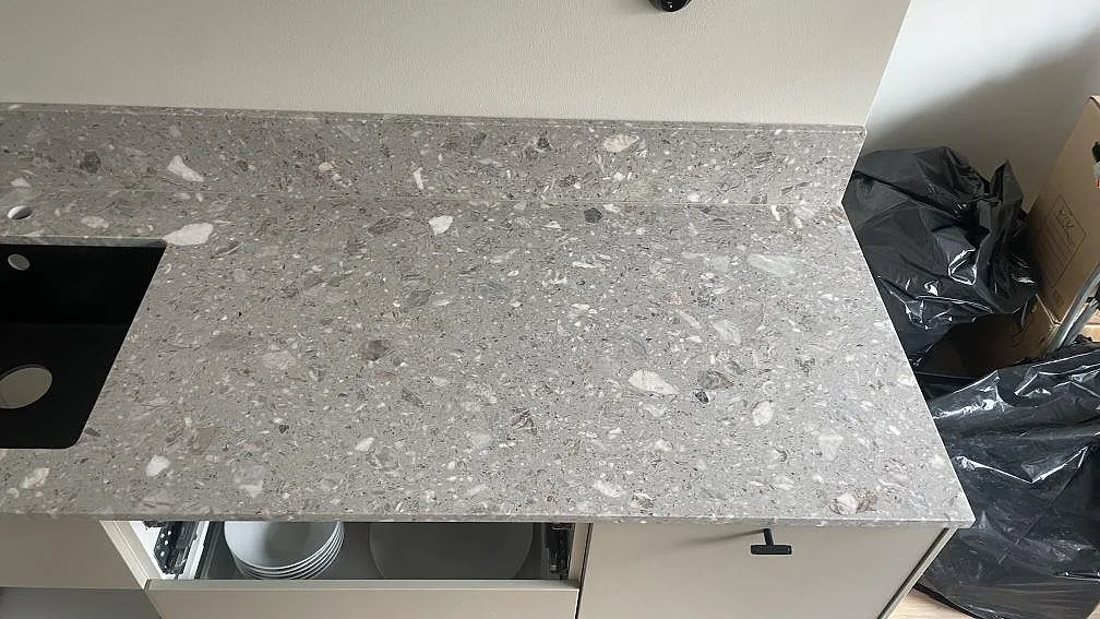 Detalj av matt Terrazzo Fior Di Pesco vid svart ho, med grå stenfragment och låg stänkkant i köket i Malmö.