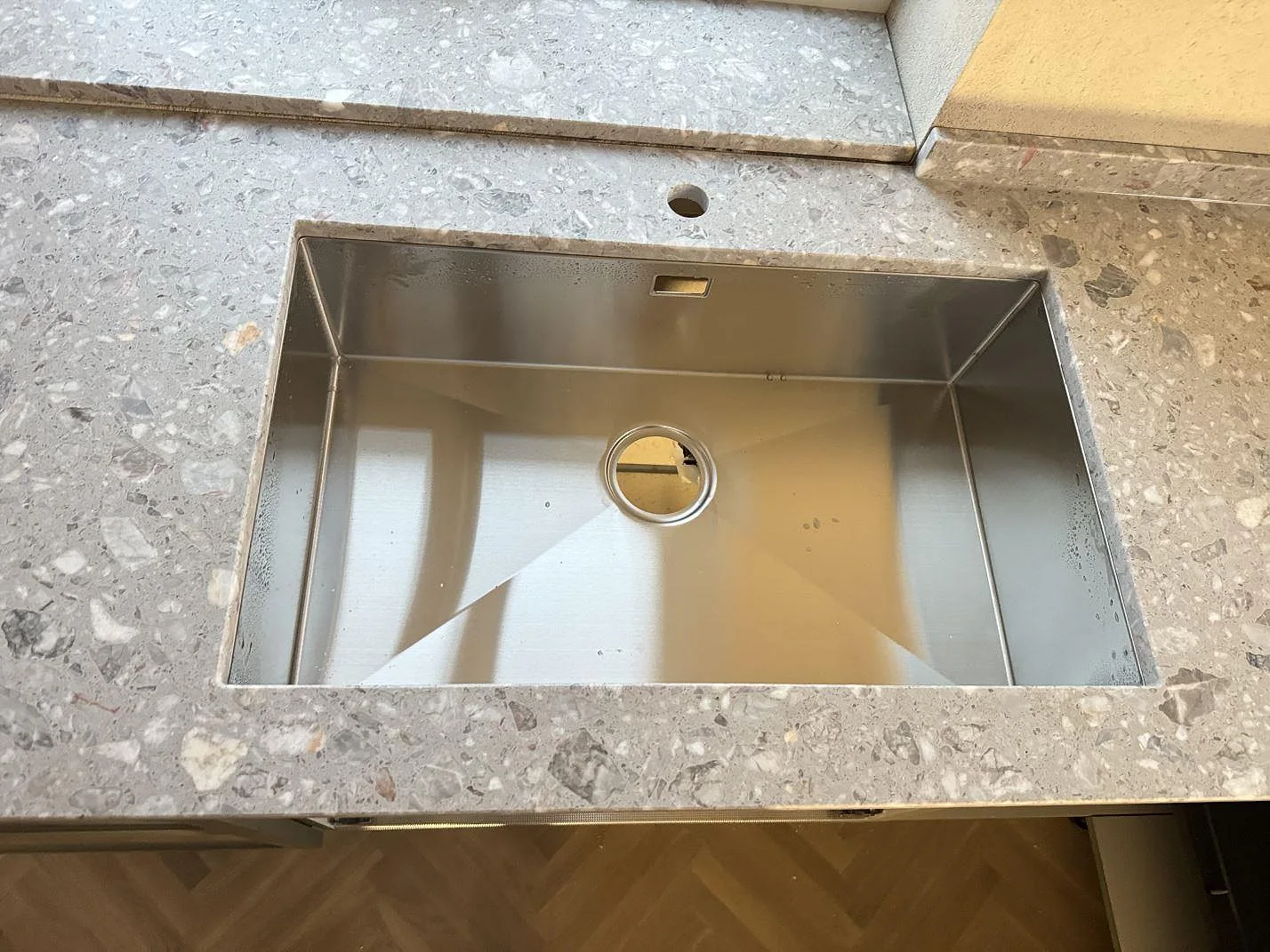 Närbild av matt Terrazzo Fior Di Pesco runt rostfri diskho och blandarhål i ett kök i Sankt olof.