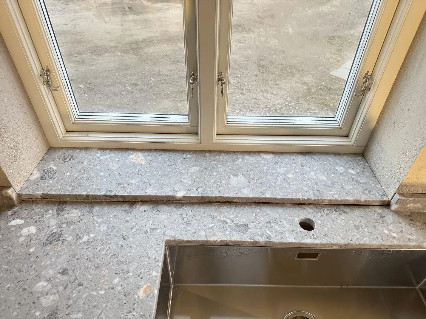 Fönsterbänk och arbetsyta i matt Terrazzo Fior Di Pesco ovanför rostfri diskho i Sankt olof.