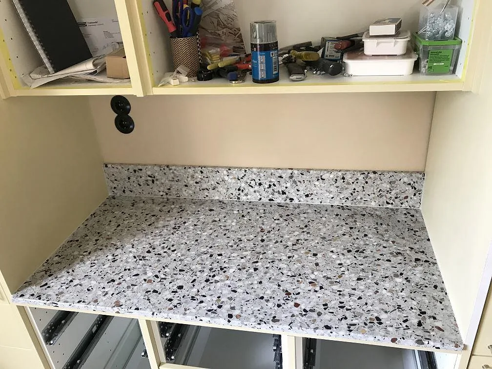 Terrazzobänkskiva i Terrazzo GV med spräckliga stenflisor och uppvikt stänkkant under köksskåp i ett kök i Göteborg.