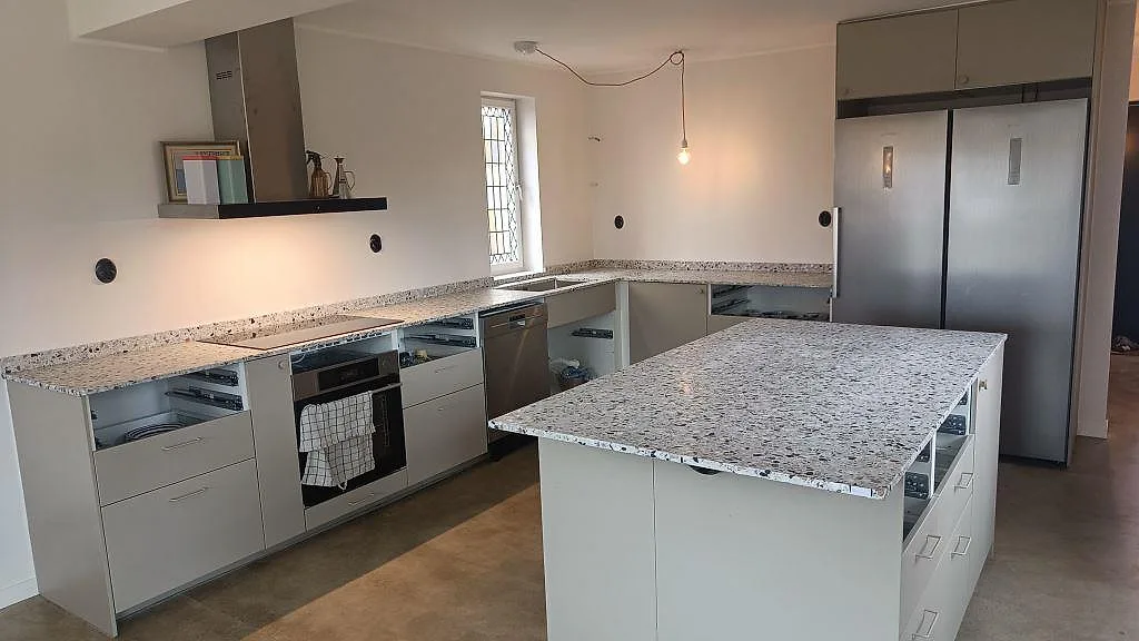 Köksbänkskiva och köksö i Terrazzo GV, Matt, med vit köksinredning och svart induktionshäll i Malmö.