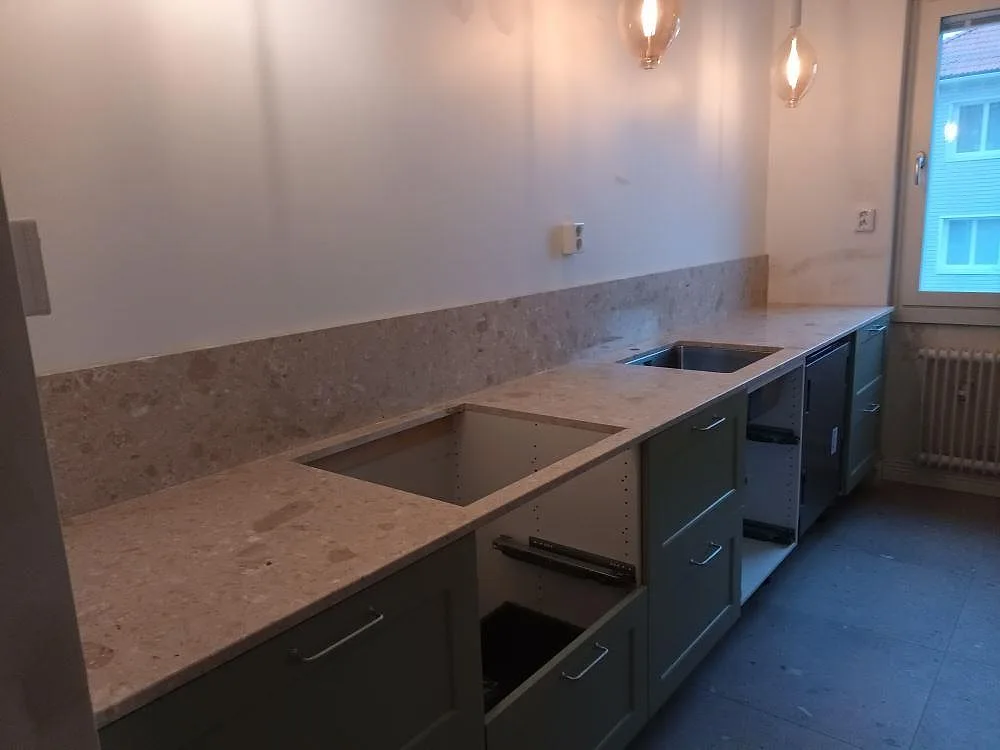 Köksbänkskiva i Terrazzo Perlato Royal, matt varmt beige marmorterrazzo, med två underlimmade diskhoar och uppvikt stänkkant i ett kök i Enköping.
