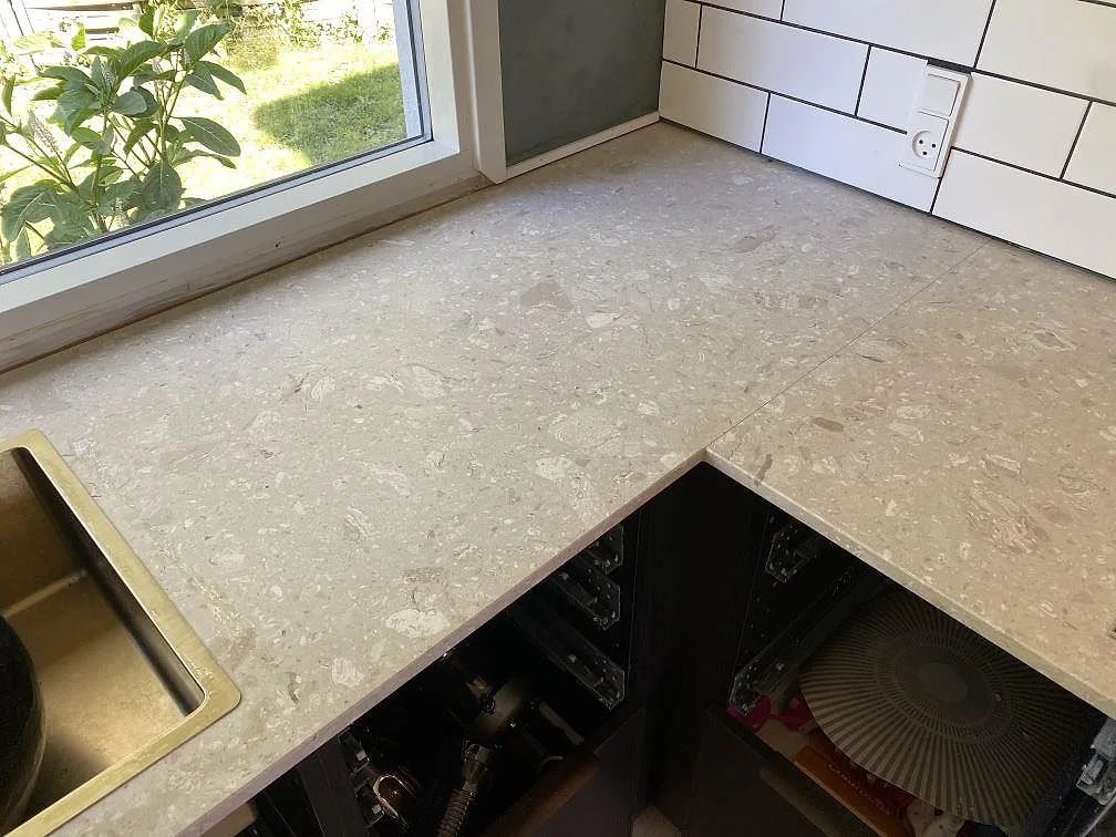 L-formad köksbänkskiva i Terrazzo Perlato Royal, matt, med mässingsfärgad diskho vid fönster i ett kök i Espergærde.