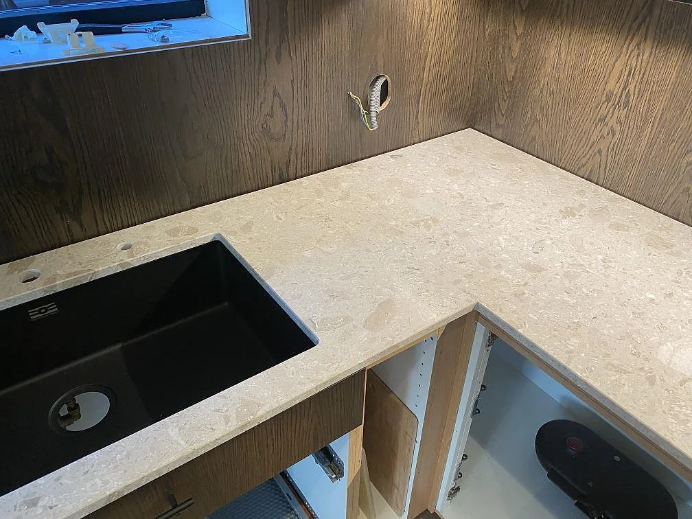 Hörnbänkskiva i Terrazzo Perlato Royal med underlimmad svart diskho mot mörk träinredning i ett kök i Höllviken.