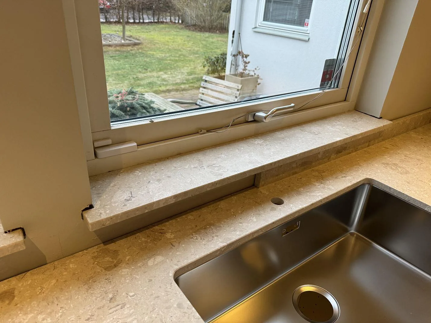 Köksbänkskiva i matt Terrazzo Perlato Royal med rostfri diskho, fönsterbänk och blandarhål vid stora fönster i Höllviken.