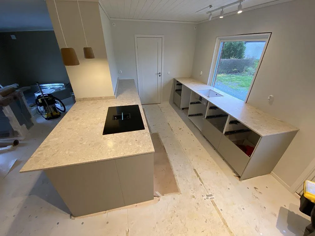 Kök i Kungsbacka med matt bänkskiva och köksö i Terrazzo Perlato Royal, svart häll och diskho vid fönstret under montering.