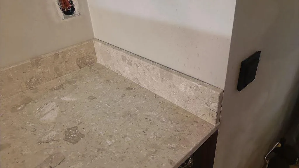 Hörn av köksbänkskiva i Terrazzo Perlato Royal, matt, med låg stänkkant intill vägg i Limhamn.