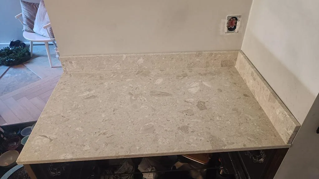 Bred detalj av kort köksbänkskiva i beige Terrazzo Perlato Royal med stänkkant under montering i Limhamn.