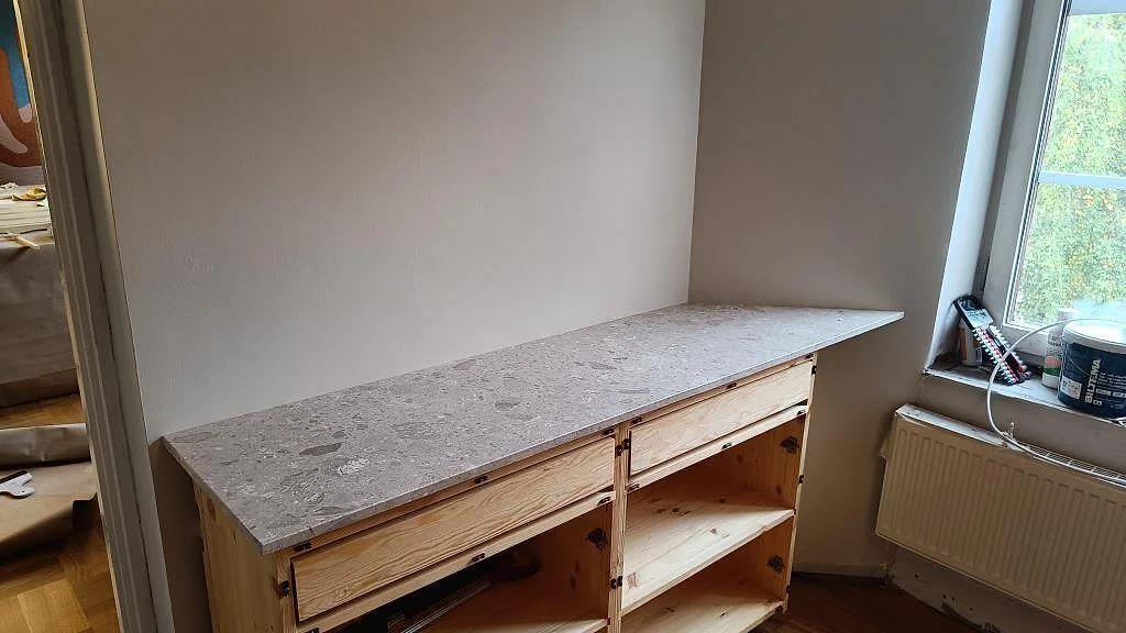 Lång köksbänkskiva i matt Terrazzo Perlato Royal på öppna trästommar intill fönster i ett kök i Malmö.
