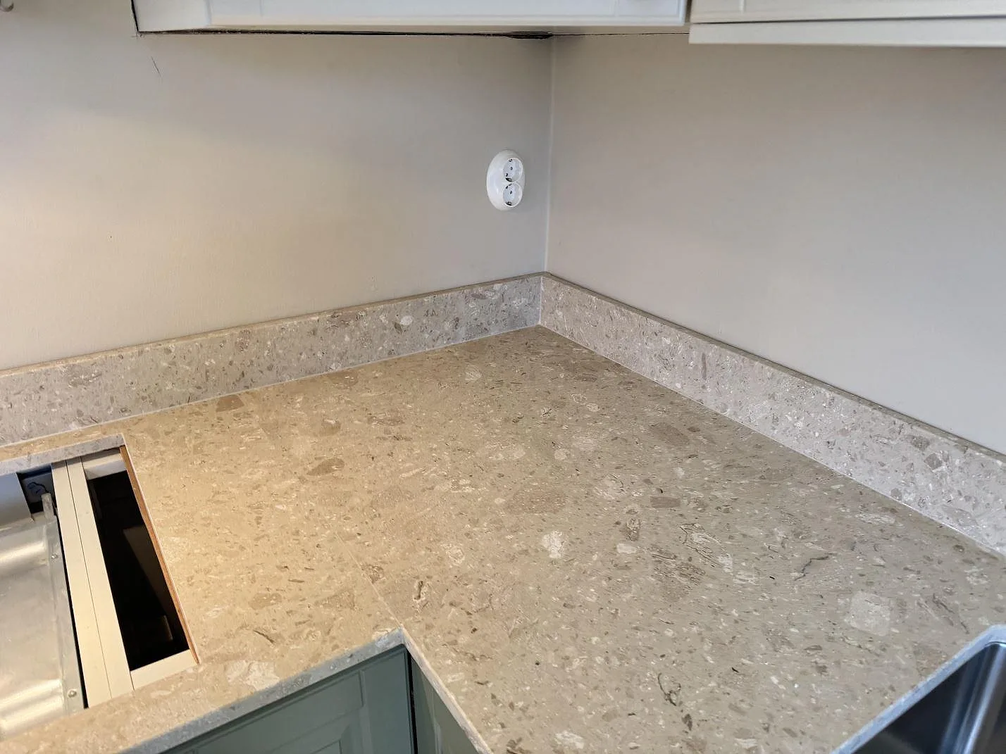 Hörnvy av köksbänkskiva i Terrazzo Perlato Royal, matt terrazzo, med stänkkant och diskho i ett kök i Malmö.