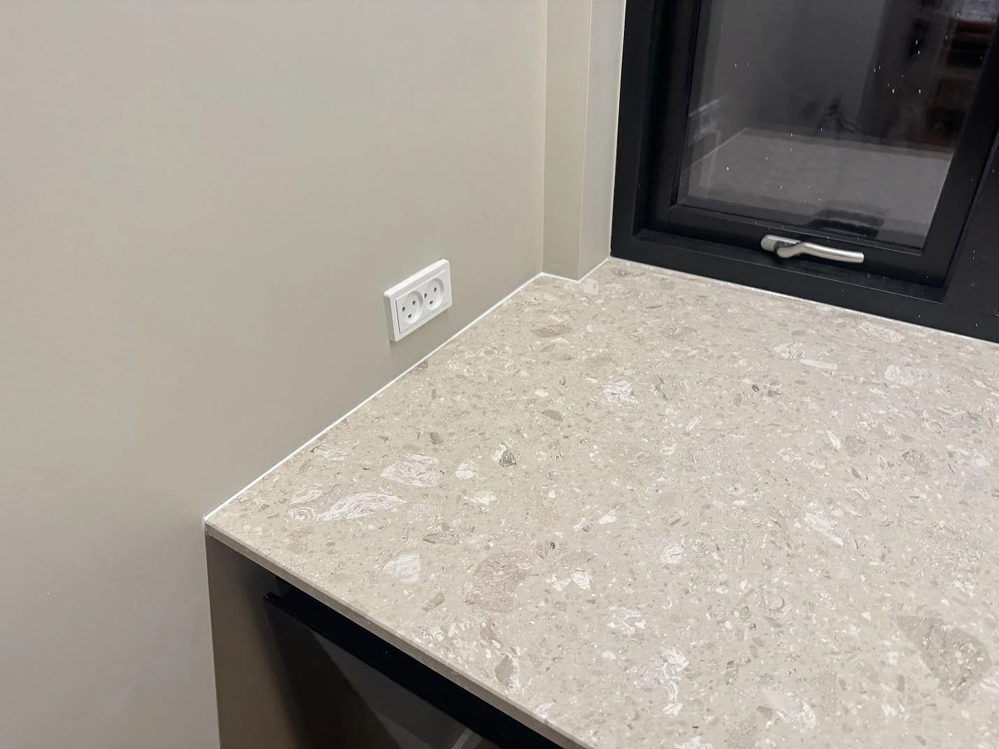 Närbild av matt Terrazzo Perlato Royal som köksbänkskiva med vägganslutning, vägguttag och svart fönsterkarm i Odense SV.