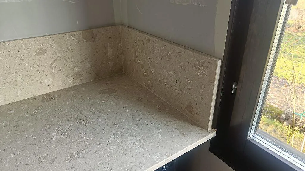 Hörndel av köksbänkskiva och stänkskydd i matt Terrazzo Perlato Royal vid fönster i Skurup.