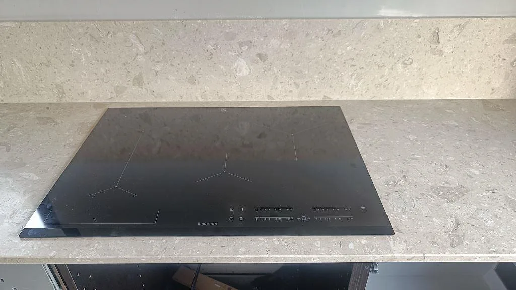 Detalj av induktionshäll i matt Terrazzo Perlato Royal med matchande stänkskydd bakom i Skurup.
