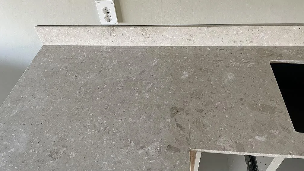 Detalj av matt köksbänkskiva i Terrazzo Perlato Royal med låg stänkkant och synliga stenkorn i ett kök i Smygehamn.