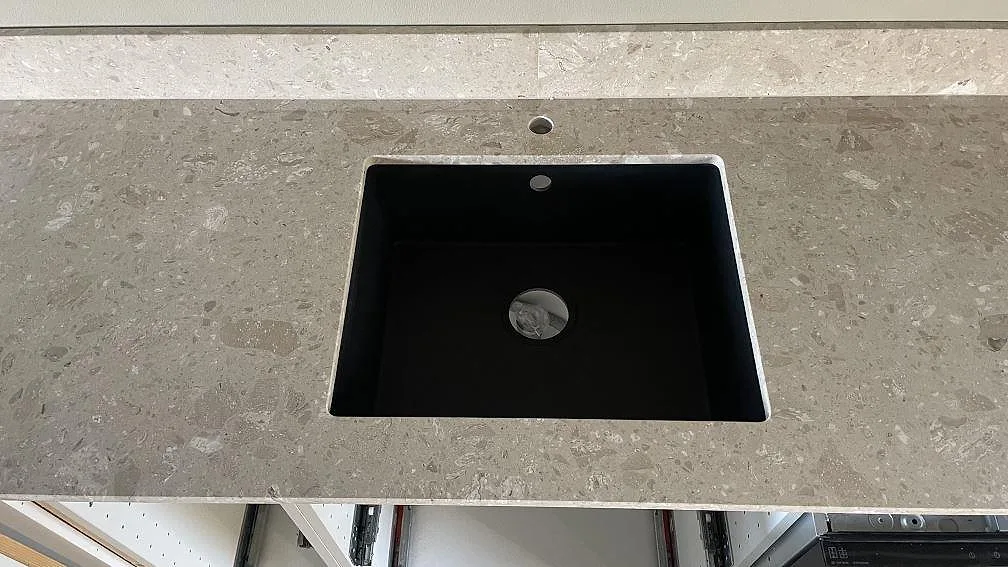 Närbild på matt Terrazzo Perlato Royal som köksbänkskiva, ljus terrazzo med svart diskho och låg stänkkant i Smygehamn.