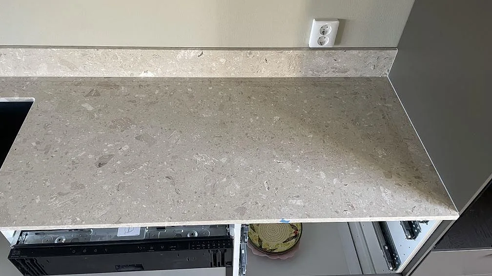 Rak del av köksbänkskiva i matt Terrazzo Perlato Royal, ljus terrazzo med uppvikt stänkkant vid högskåp i Smygehamn.