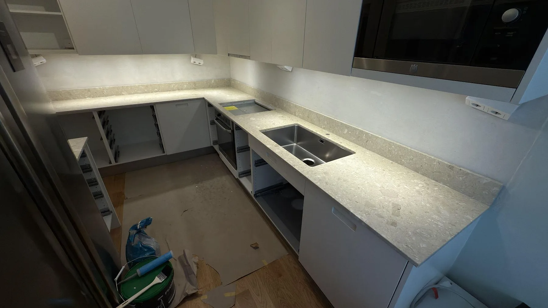 L-formad köksbänkskiva i matt Terrazzo Perlato Royal med stänkkant och monterad diskho under köksmontering i Solna.