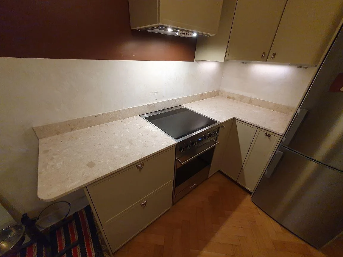 Köksbänkskiva i beige Terrazzo Perlato Royal, matt 20 mm, med låg stänkkant runt en spis i ett kök i Stockholm.