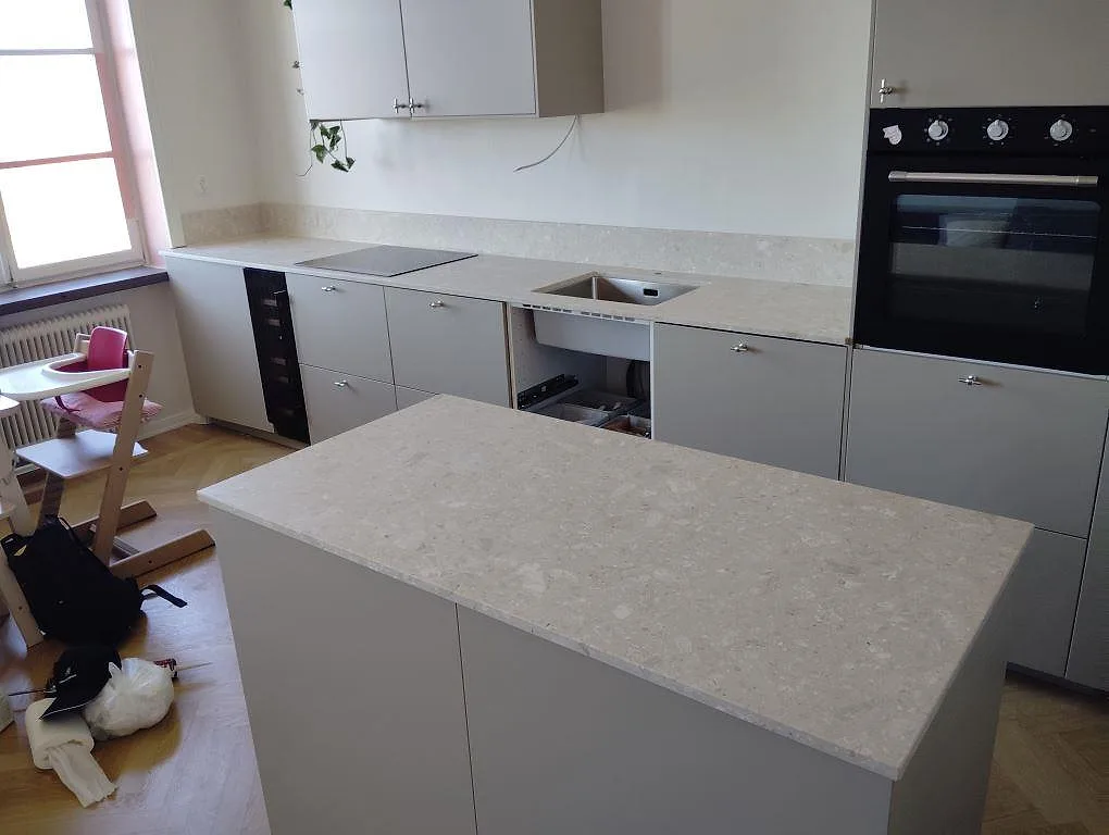 Köksbänkskiva och halvö i ljus Terrazzo Perlato Royal, matt 20 mm terrazzo, med häll, diskho och stänkkant i ett kök i Stockholm.