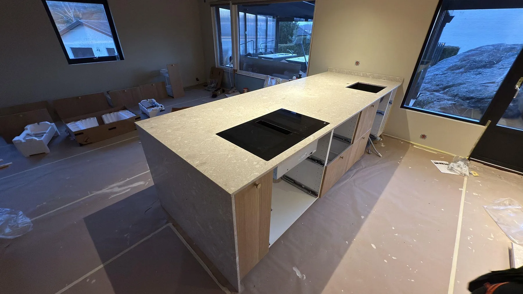 Köksö i Terrazzo Perlato Royal sedd från sidan med infälld induktionshäll och håltagning för diskho, i ett ljust kök med stora fönster under inredning i Tyresö.