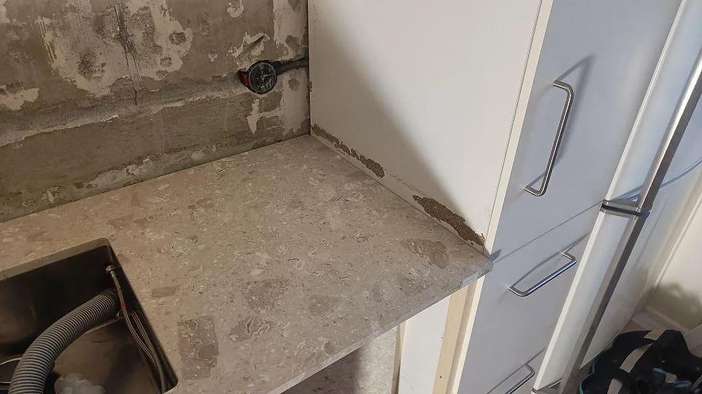 Hörn av köksbänkskiva i matt Terrazzo Perlato Royal med rostfri diskho och vita skåp under montering i Ystad.