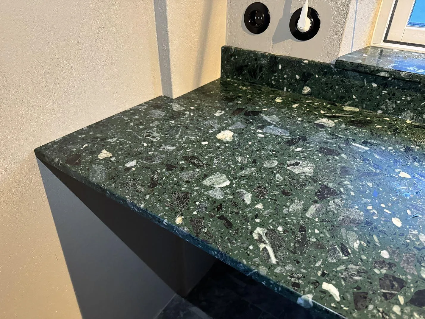 Matt grön Terrazzo Verde Alpi som köksbänkskiva med låg stänkkant och synliga stora stenfragment i Borrby.